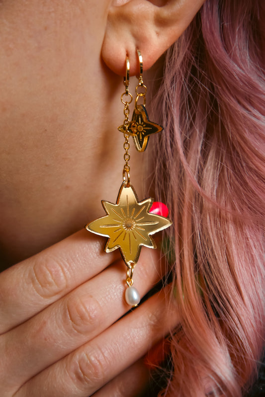 a pair of gold star earrings on a persons ear with pink hair