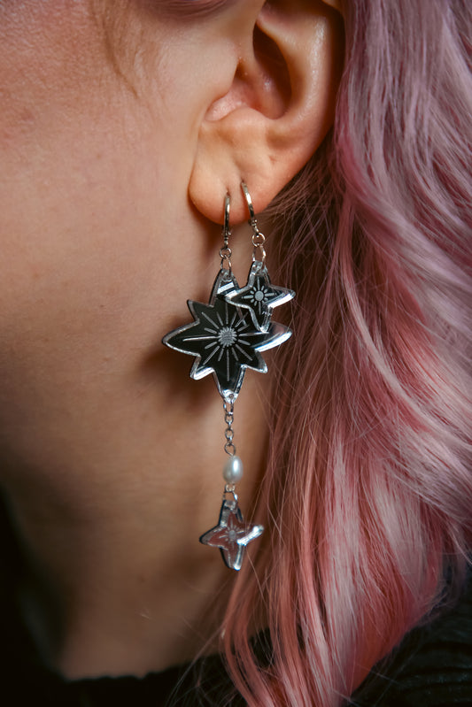a pair of silver star earrings on a persons ear with pink hair