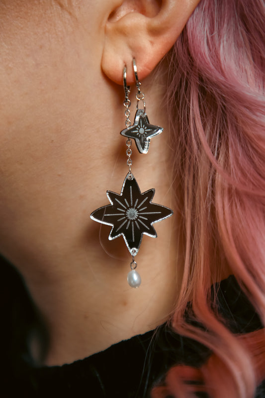 a pair of silver star earrings on a persons ear with pink hair