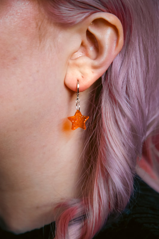 A transparent glitter orange star acrylic earring on an ear