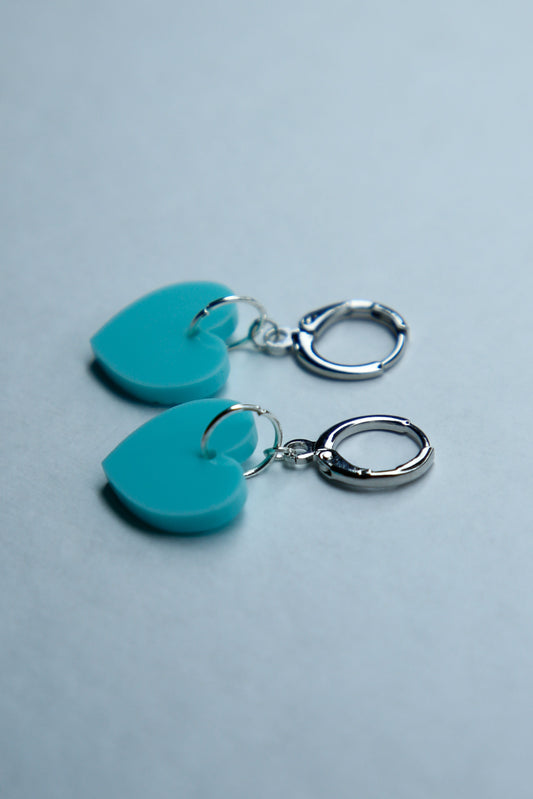 A pair of pastel blue heart acrylic earring on a blue background