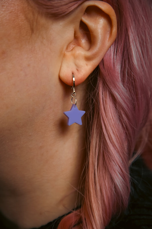 A pastel purple star acrylic earring on an ear