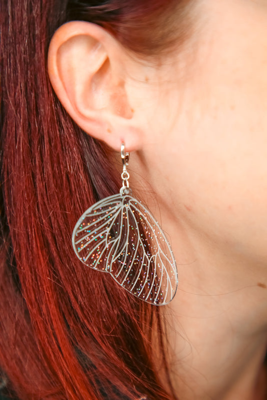 glitter transparent fairy wing acrylic earring on a persons ear with brown hair behind