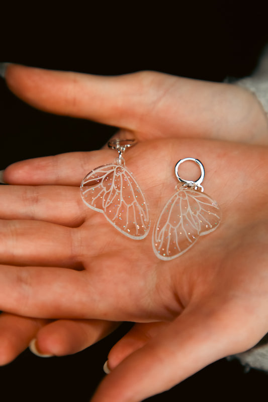 mini glitter transparent fairy wing acrylic earring on a persons ear with brown hair behind