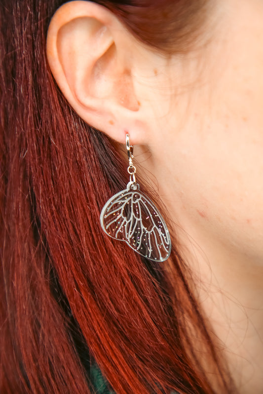 mini glitter transparent fairy wing acrylic earring on a persons ear with brown hair behind