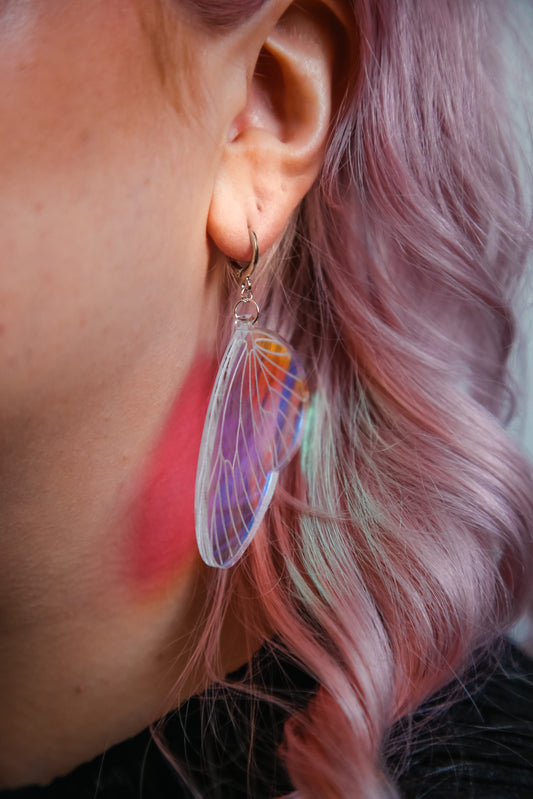 An iridescent acrylic earring styled after a fairies wing against pink hair
