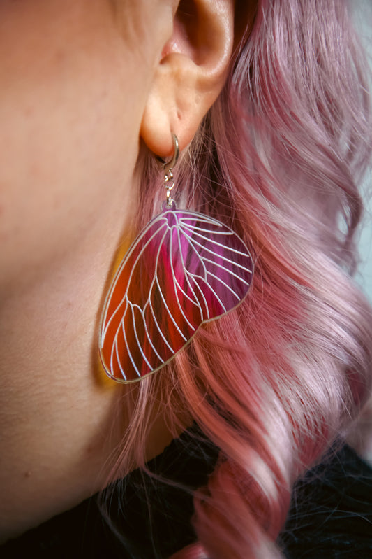 An iridescent acrylic earring styled after a fairies wing against pink hair