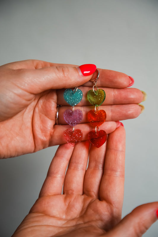 multi coloured heart acrylic earrings being held by hands