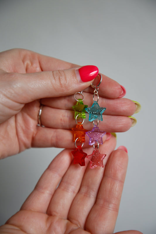 multicoloured glittery transparent star acrylic earrings being held by hands
