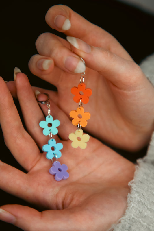 a pair of multi coloured pastel flower acrylic earrings being held by a hand