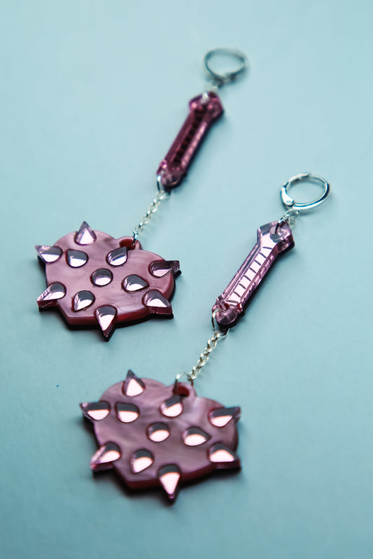 a pair of pink mace acrylic earrings with pink heart shaped mace ball and reflective pink handle and spikes on a blue background