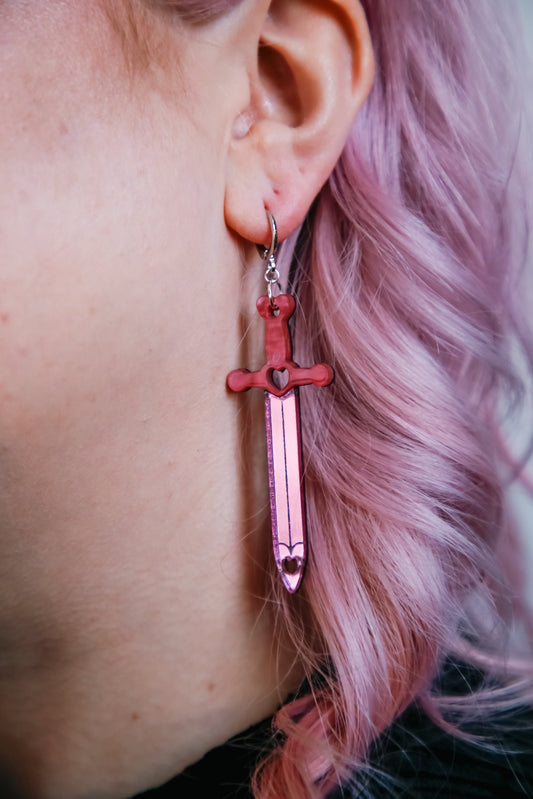 Pink sword acrylic earring with a reflective pink blade against pink hair