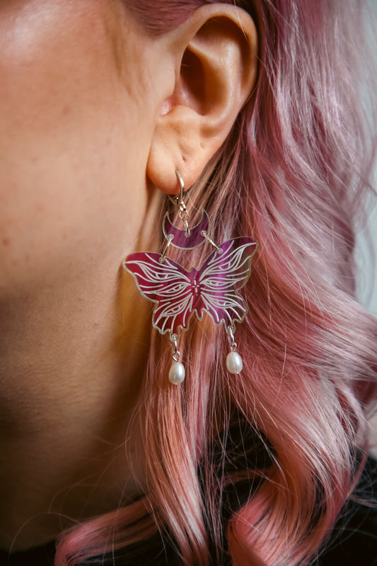 small iridescent butterfly acrylic earring with pearls on a persons ear with pink hair