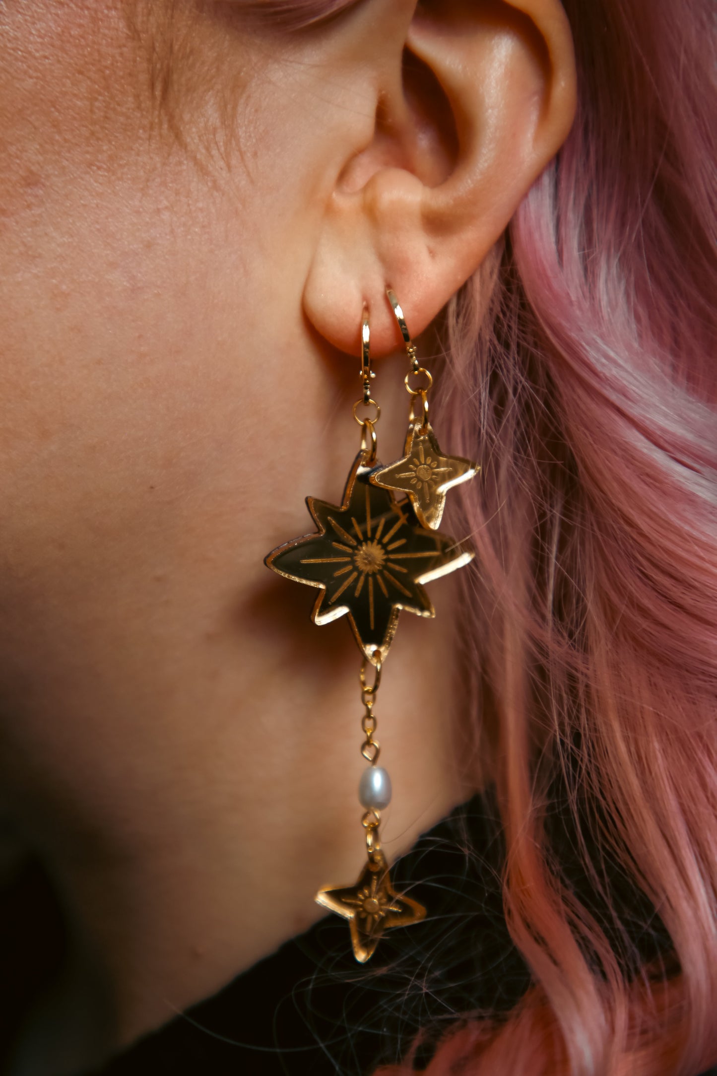 a pair of gold star earrings on a persons ear with pink hair