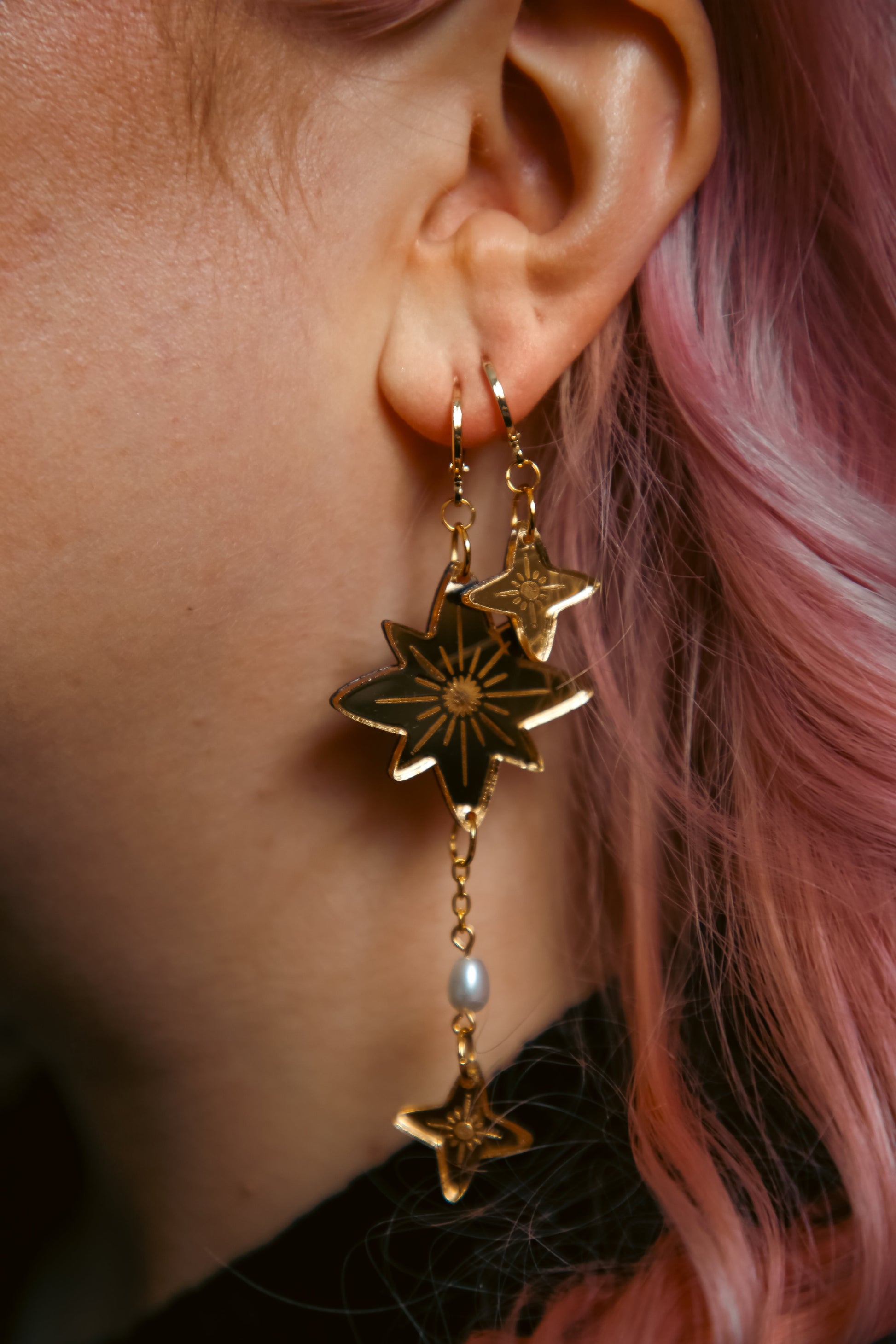 a pair of gold star earrings on a persons ear with pink hair
