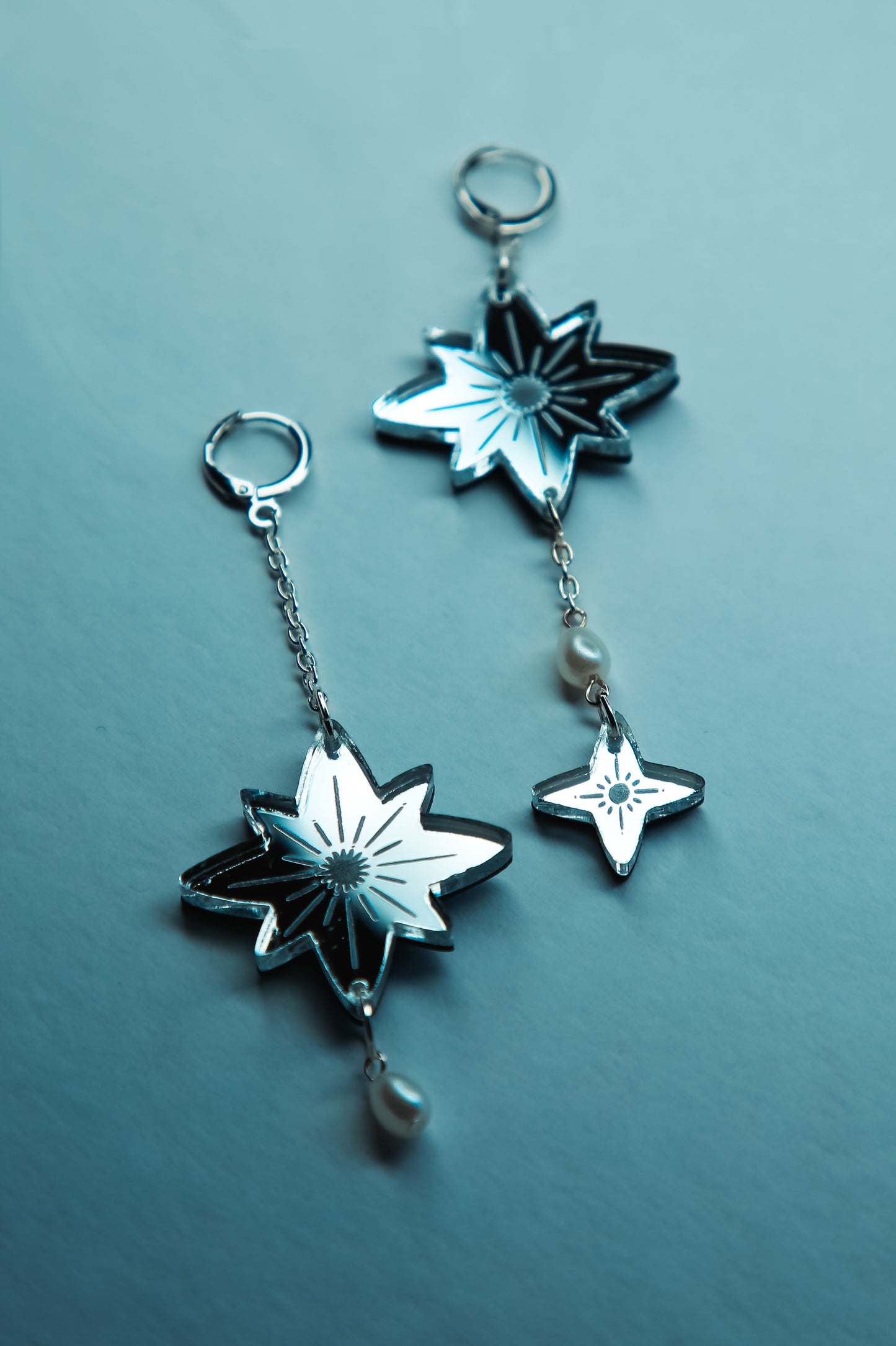 a pair of large star acrylic earrings with silver reflective material and pearls