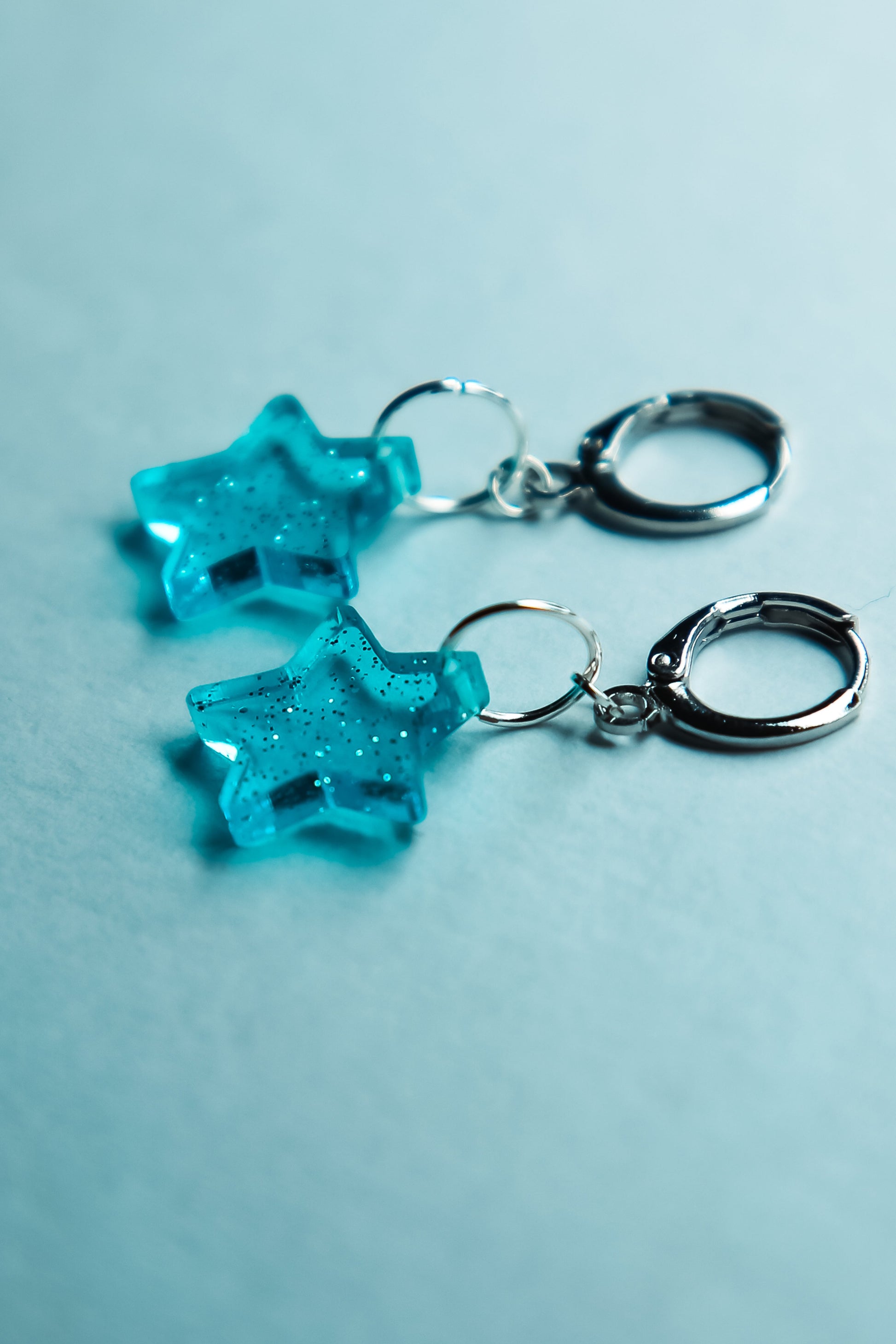 A pair of transparent glitter blue star acrylic earring against a blue background