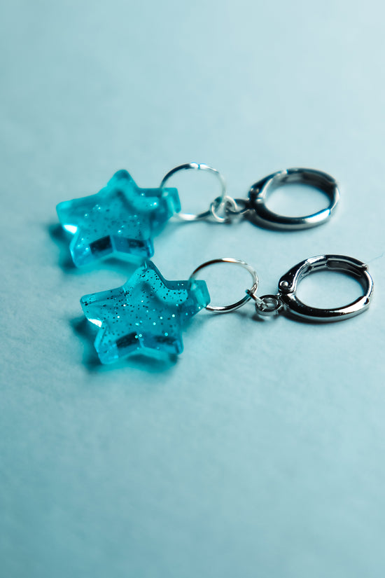 A pair of transparent glitter blue star acrylic earring against a blue background
