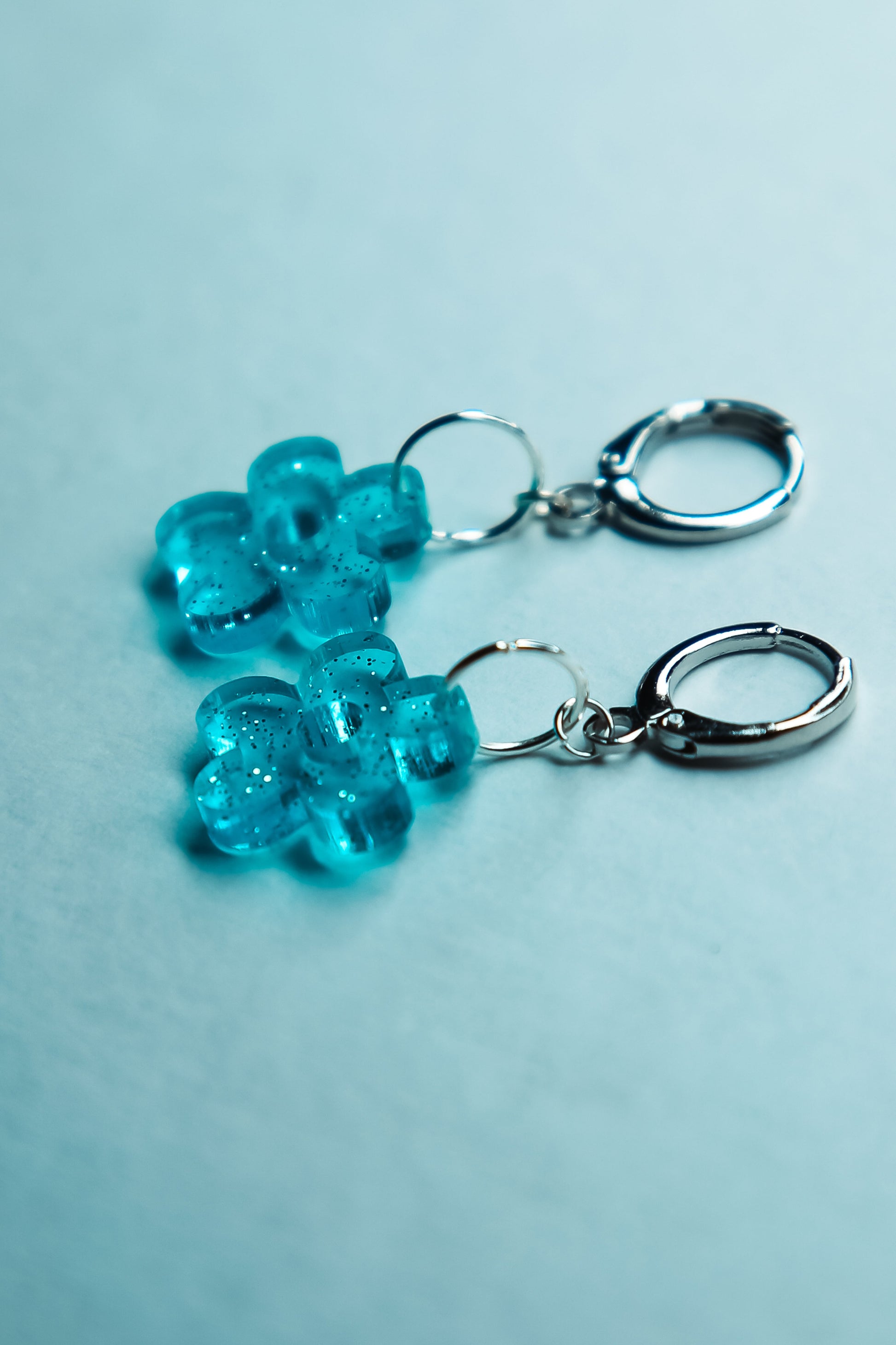 A pair of transparent glitter blue flower acrylic earring against a blue background