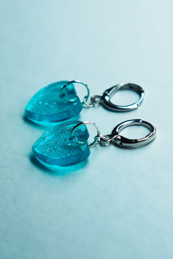 A pair of transparent glitter blue heart acrylic earring against a blue background