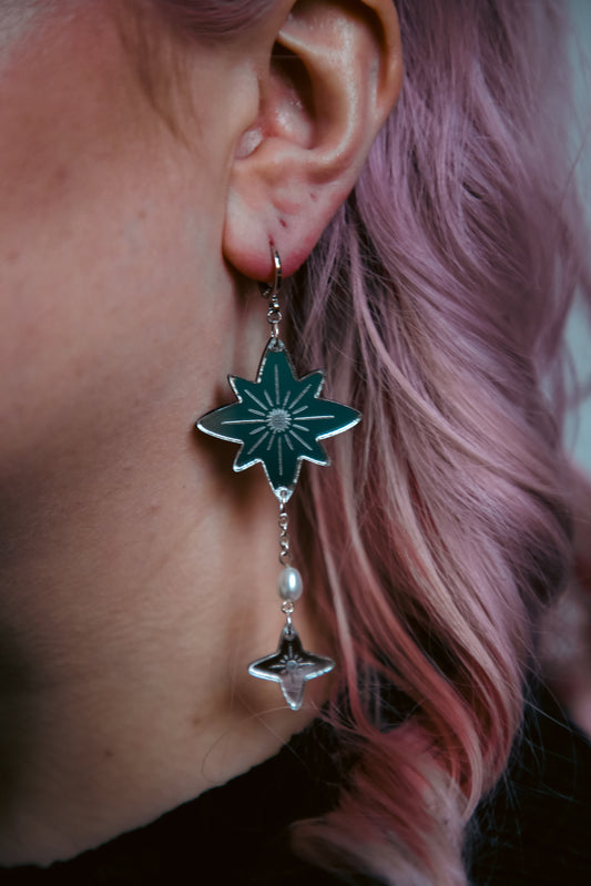 large star acrylic earrings with silver reflective material and a pearl against pink hair