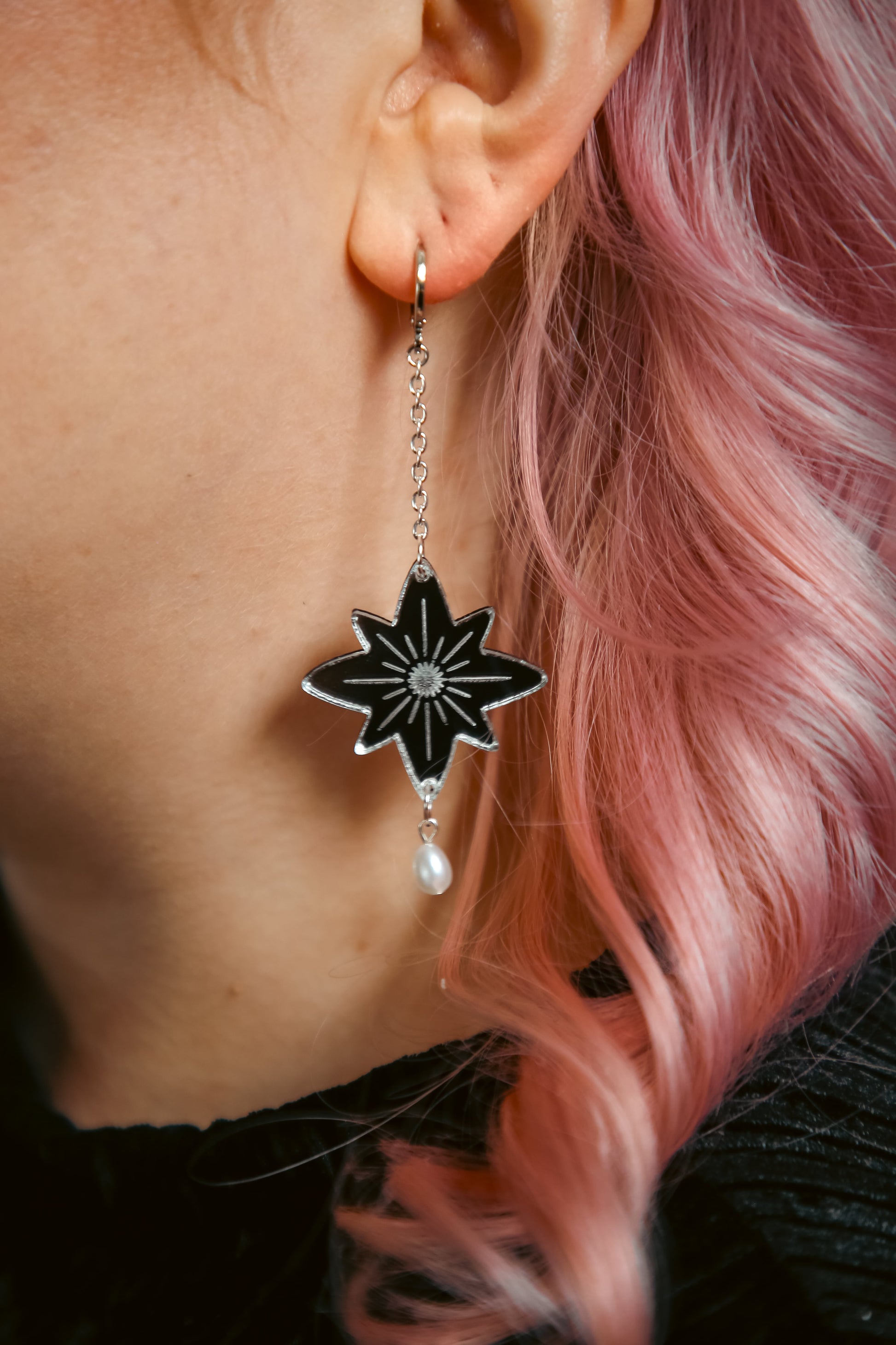 large star acrylic earrings with silver reflective material and a pearl against pink hair