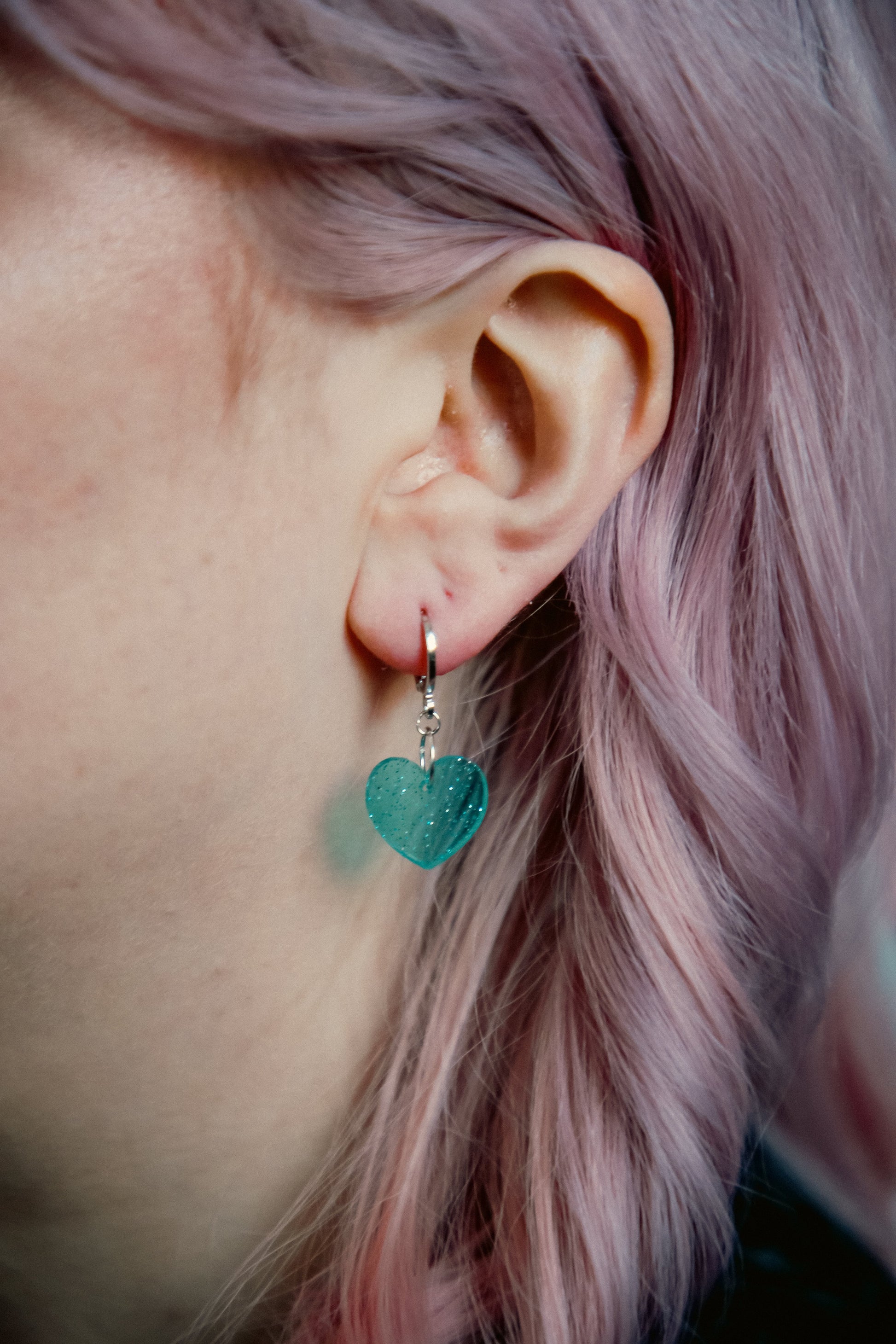 transparent glitter blue heart acrylic earring against pink hair