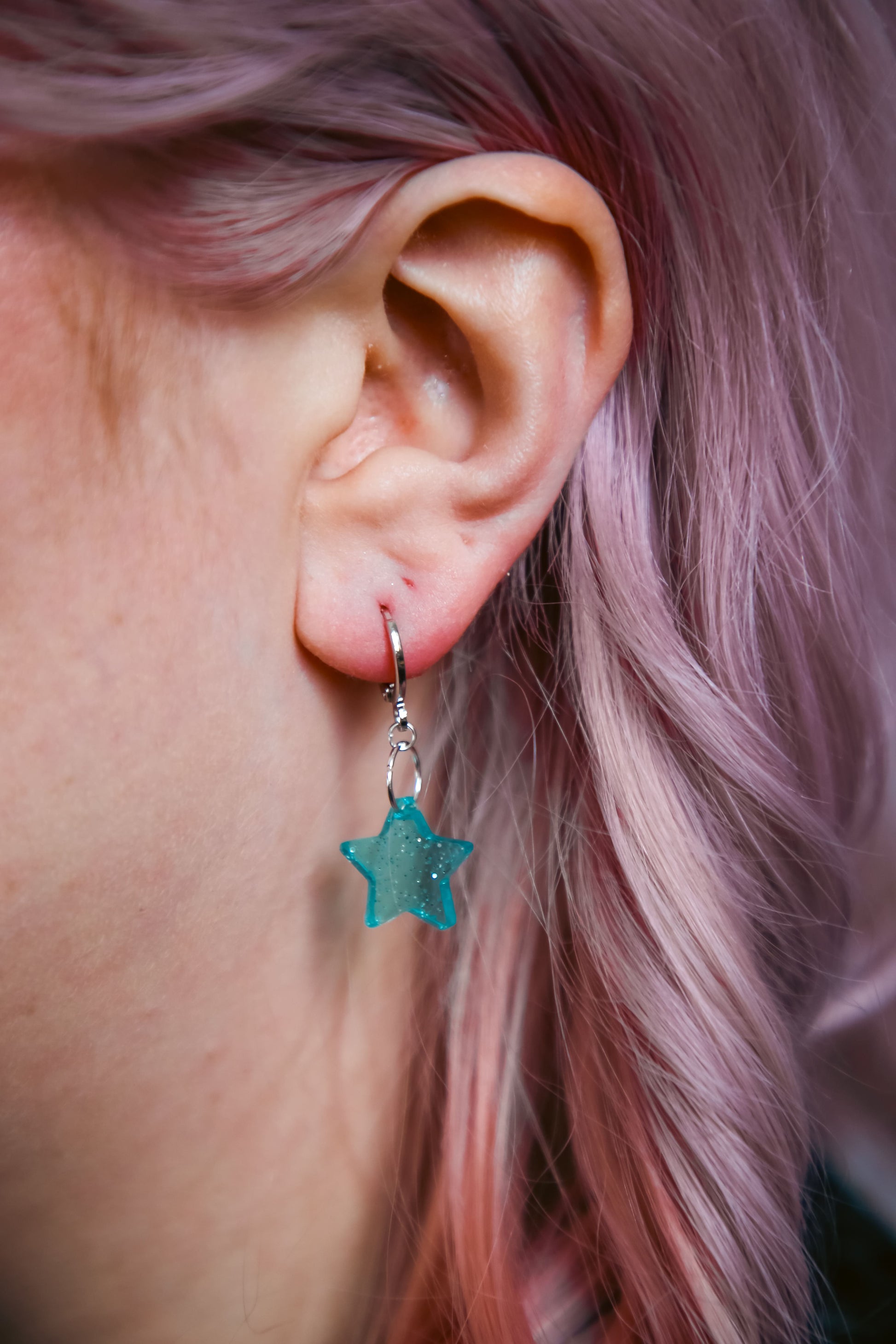A transparent glitter blue star acrylic earring against a model with pink hair