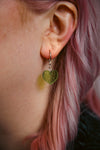 A transparent glitter green heart acrylic earring against a model with pink hair