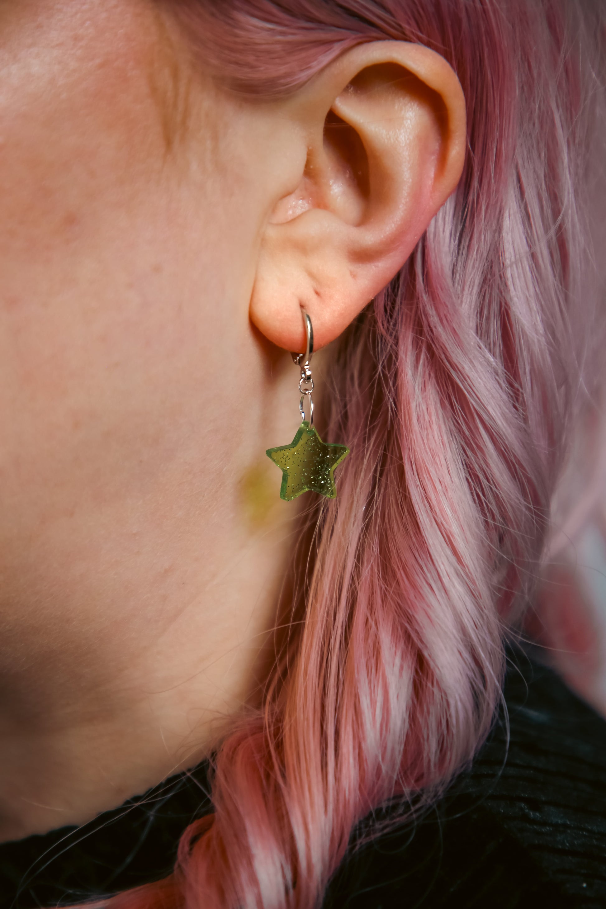 A glitter green star acrylic earring on a persons ear