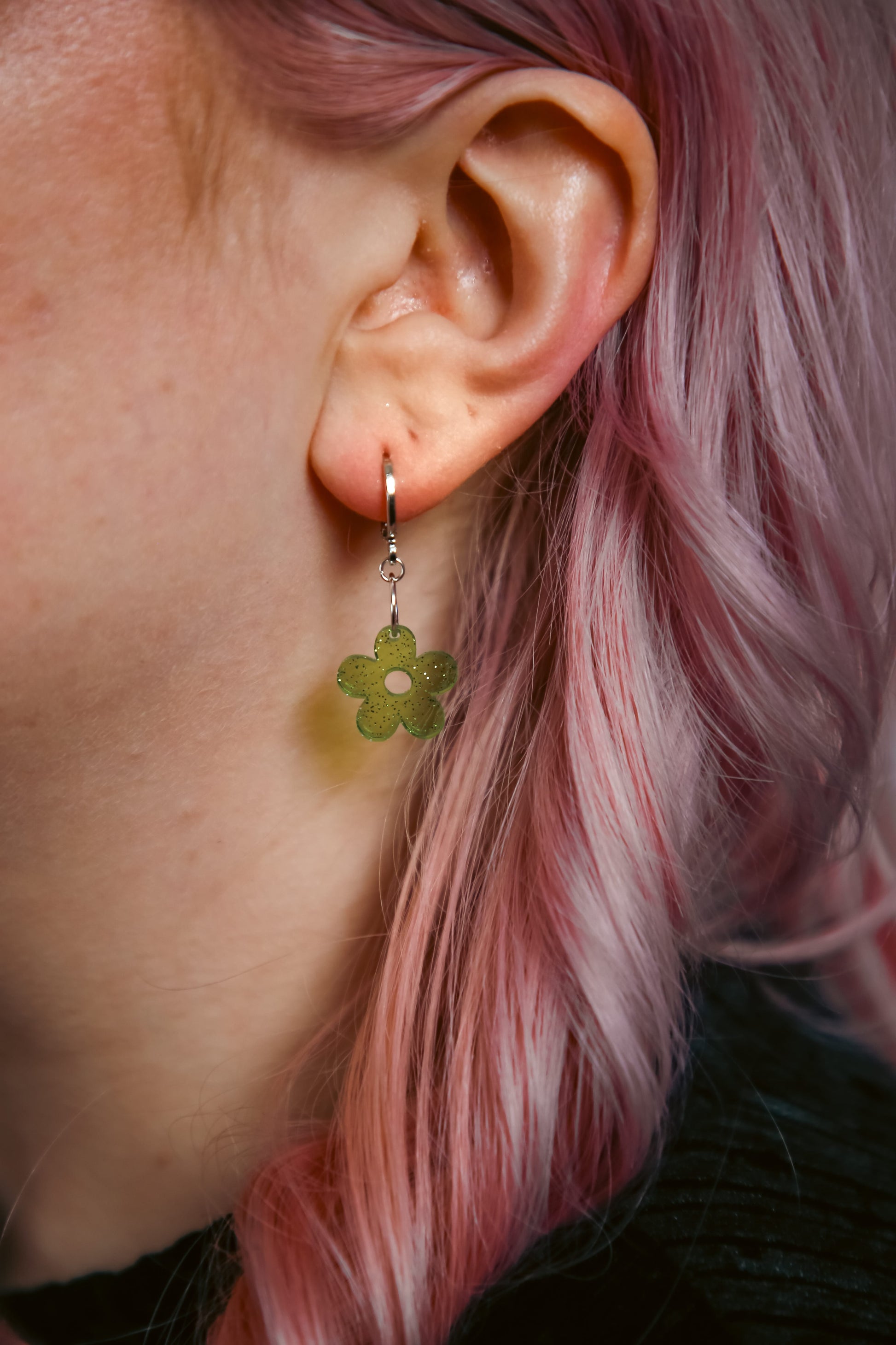 A transparent glitter green flower acrylic earring on a persons ear
