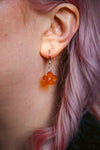 A transparent glitter orange flower acrylic earring on an ear