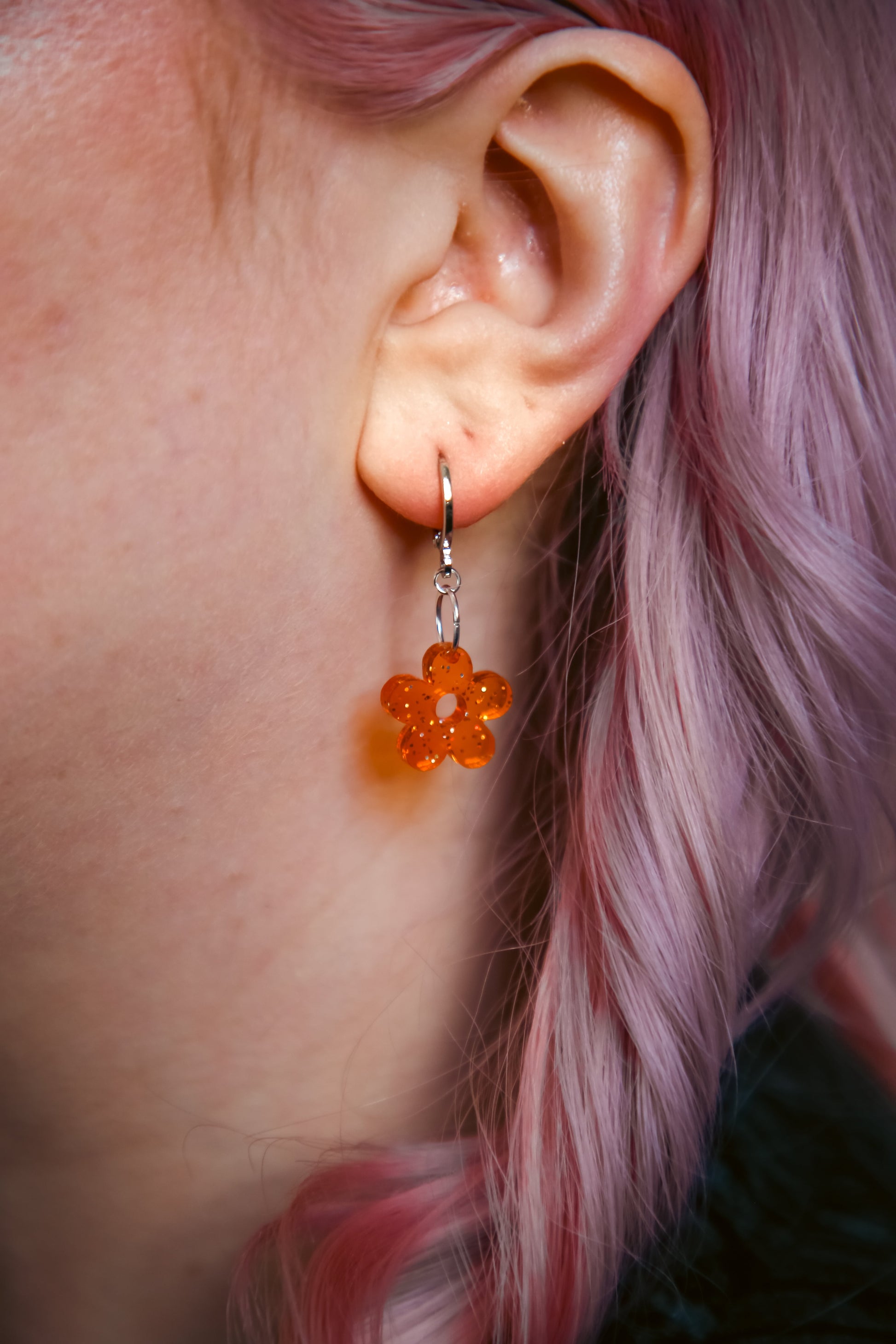 A transparent glitter orange flower acrylic earring on an ear