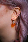 A transparent glitter orange heart acrylic earring on an ear