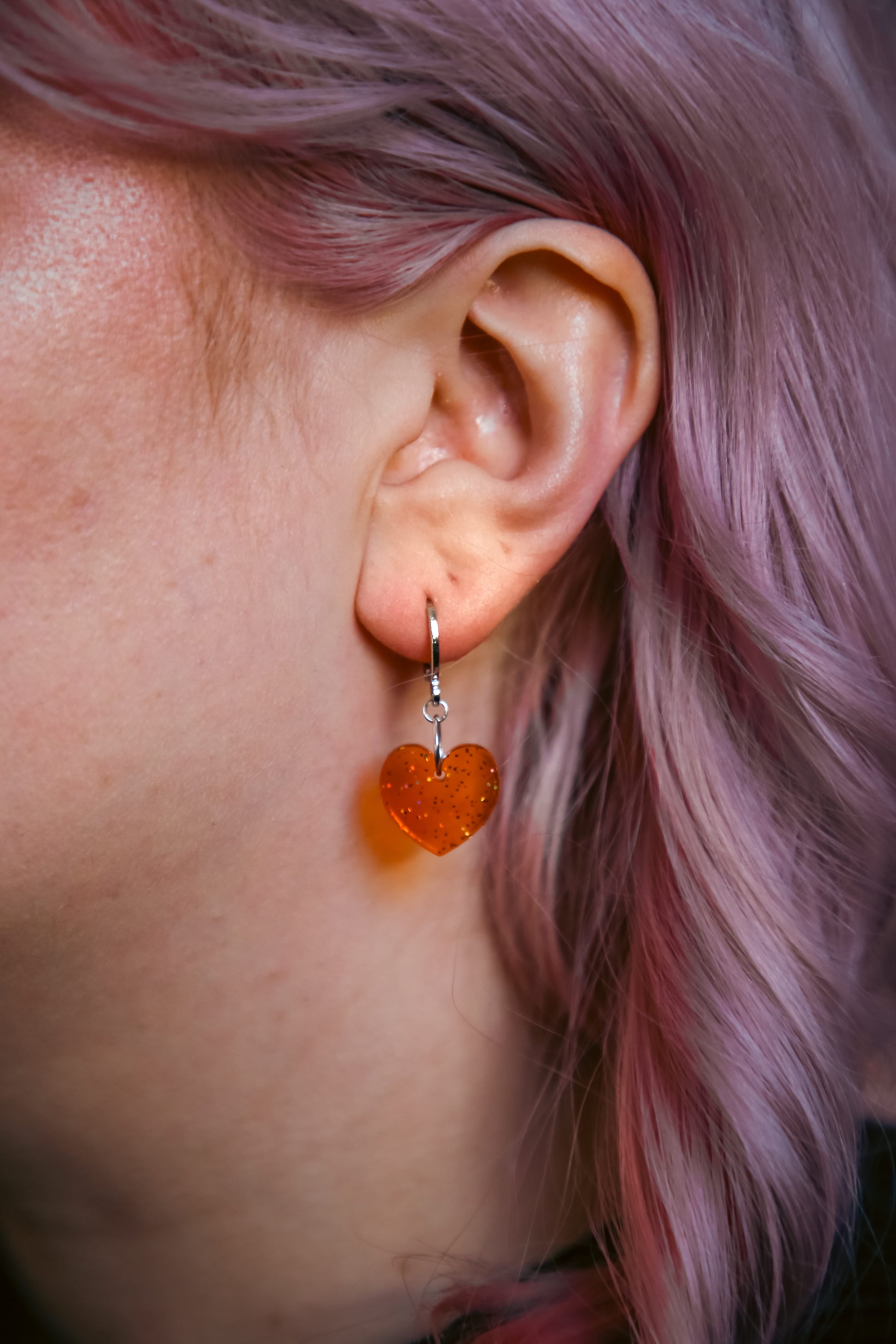 A transparent glitter orange heart acrylic earring on an ear