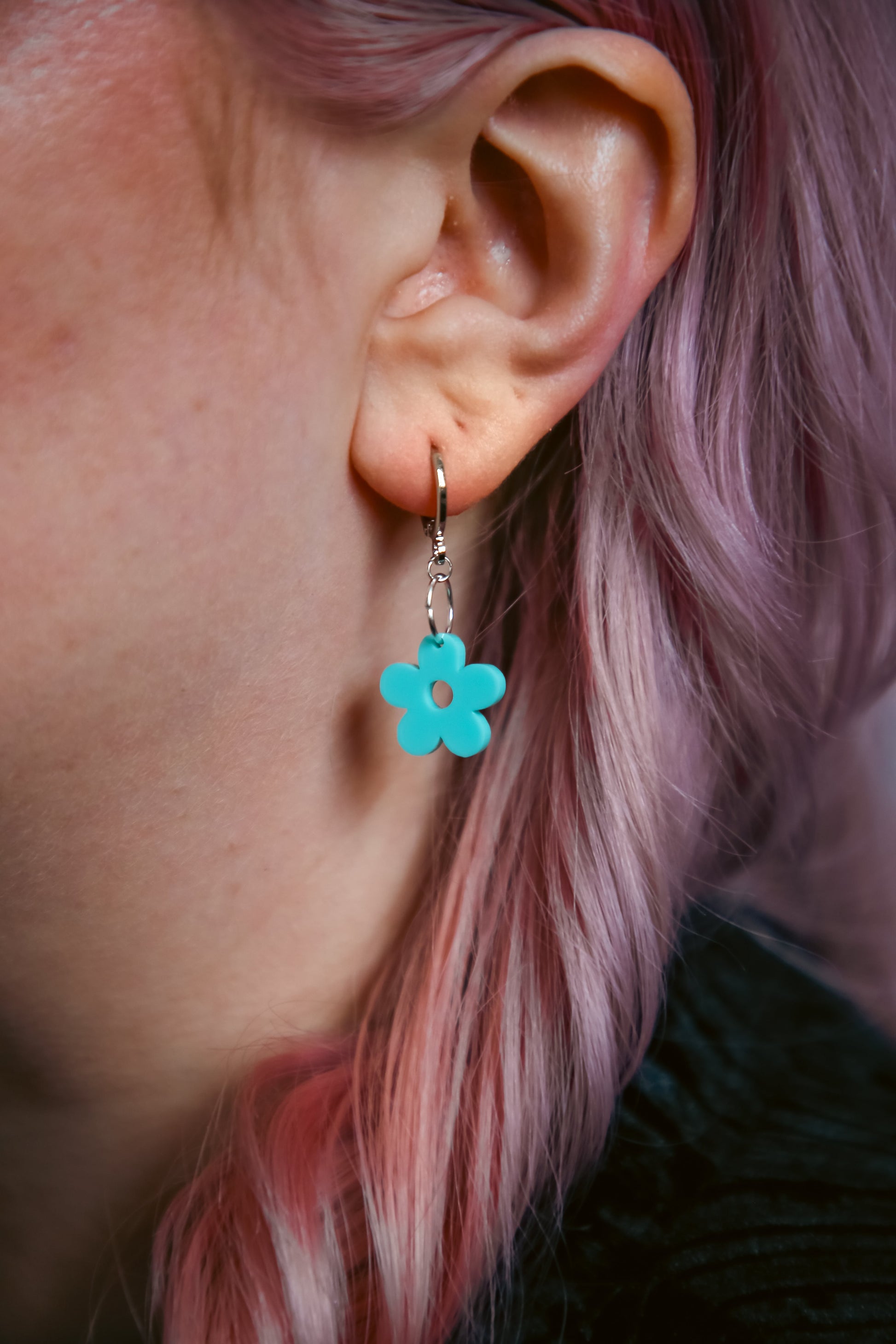 A pastel blue flower acrylic earring on an ear