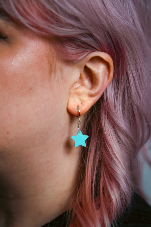 A pastel blue star acrylic earring on an ear