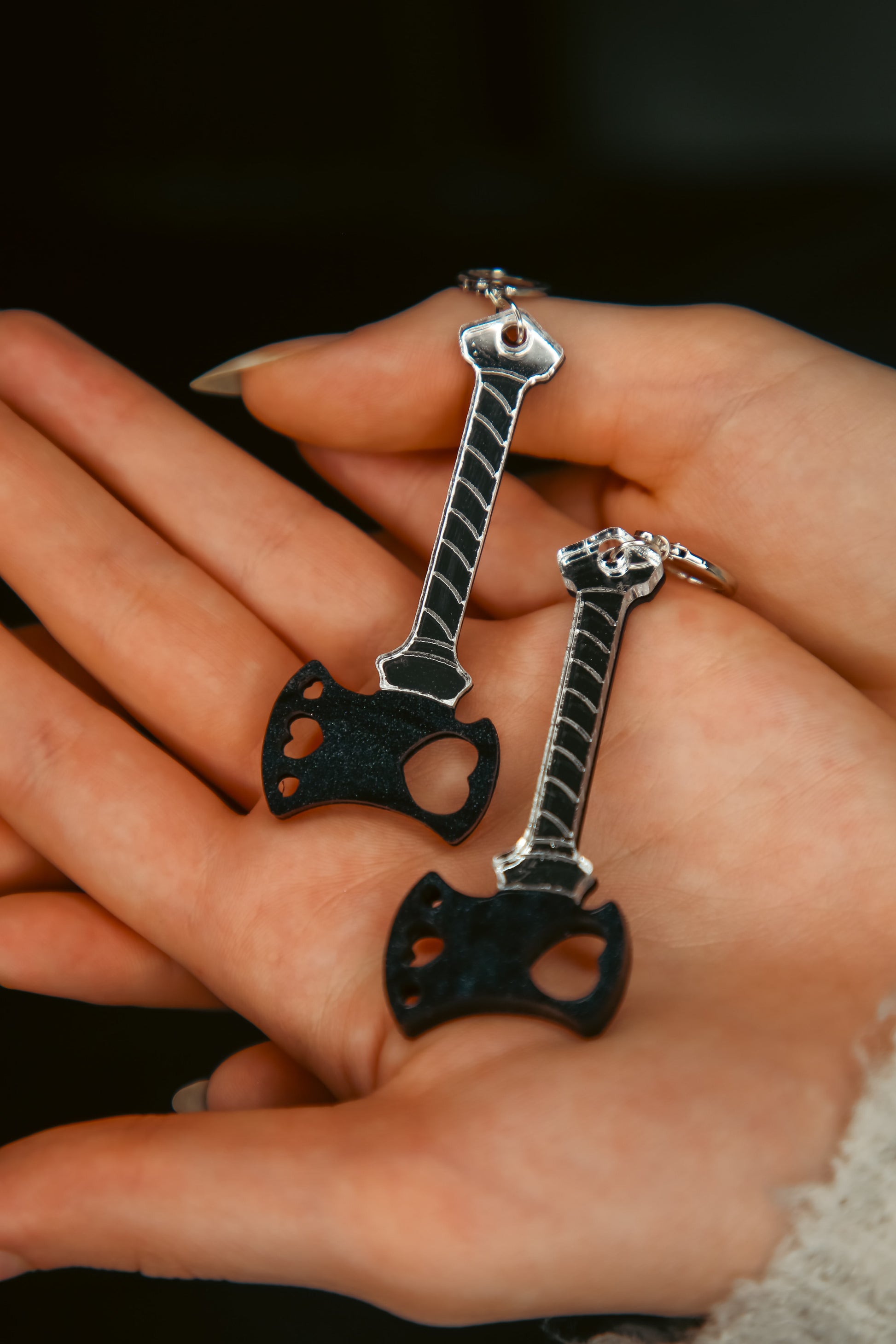 a pair of black axe with a reflective silver handle acrylic earrings in a persons hands