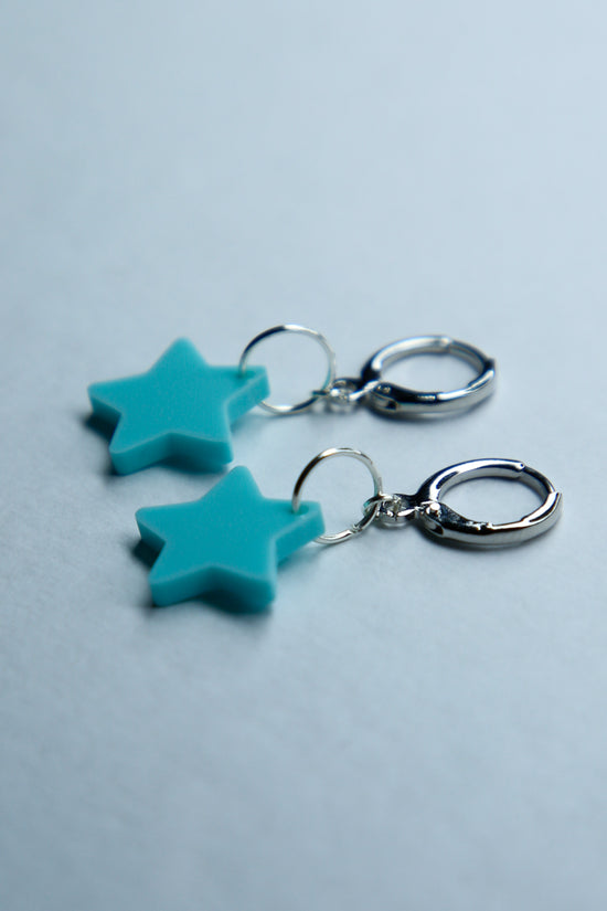 A pair of pastel blue flower acrylic earring on a blue background