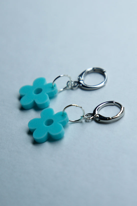 A pair of pastel blue flower acrylic earrings on a blue background