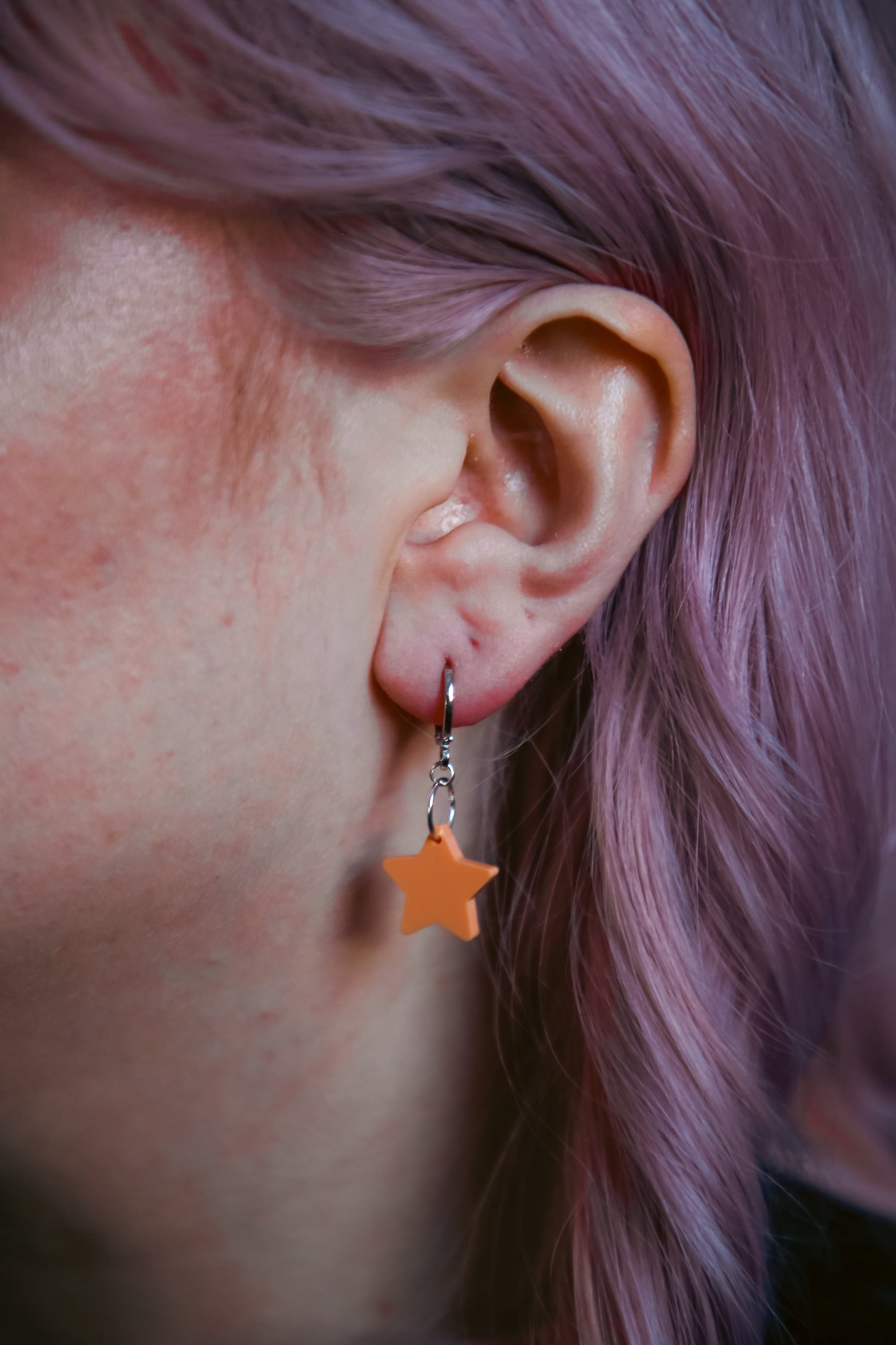 A pastel orange star acrylic earring on an ear