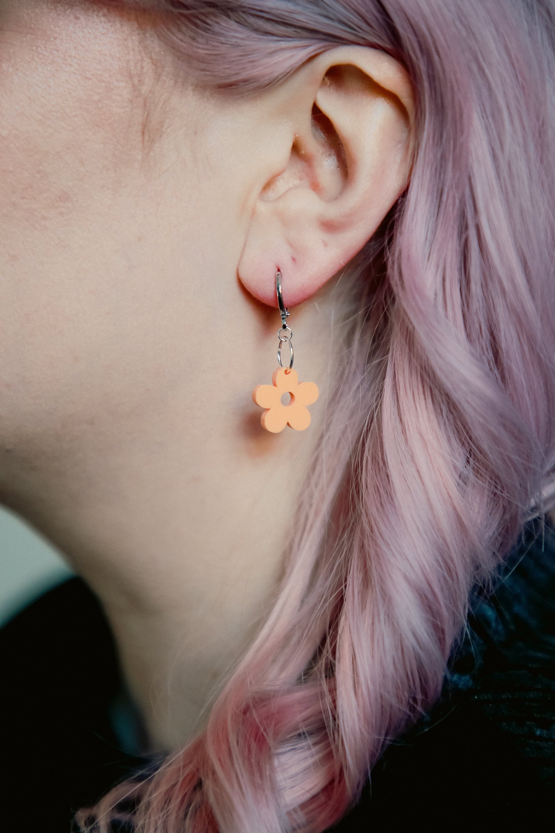 A pastel orange flower acrylic earring on an ear