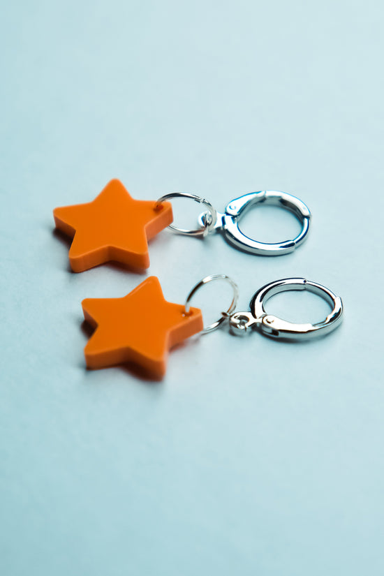 A pair of pastel orange star acrylic earring on a blue background