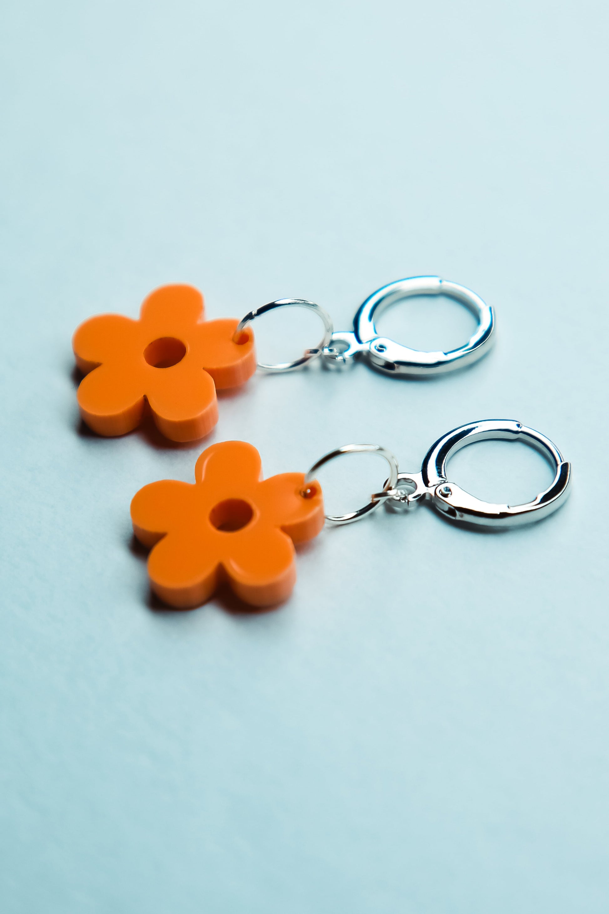 A pair of pastel orange heart acrylic earring on a blue background