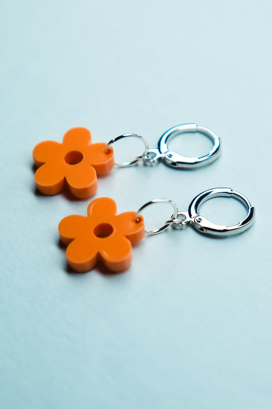 A pair of pastel orange heart acrylic earring on a blue background