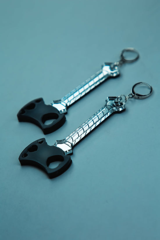a flat lay of a pair of black blade and reflective silver handle axe acrylic earrings 