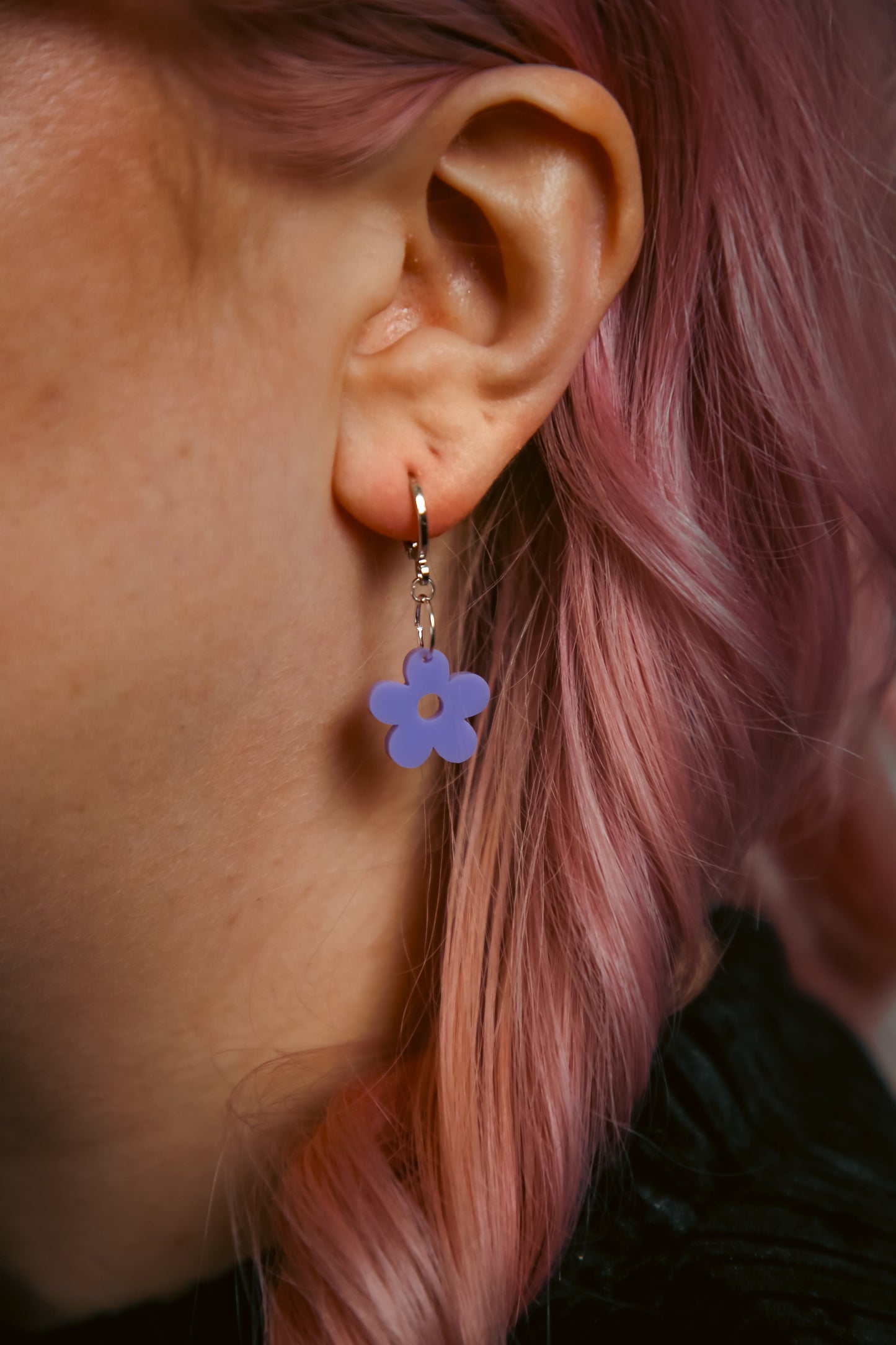 A pastel purple flower acrylic earring on an ear