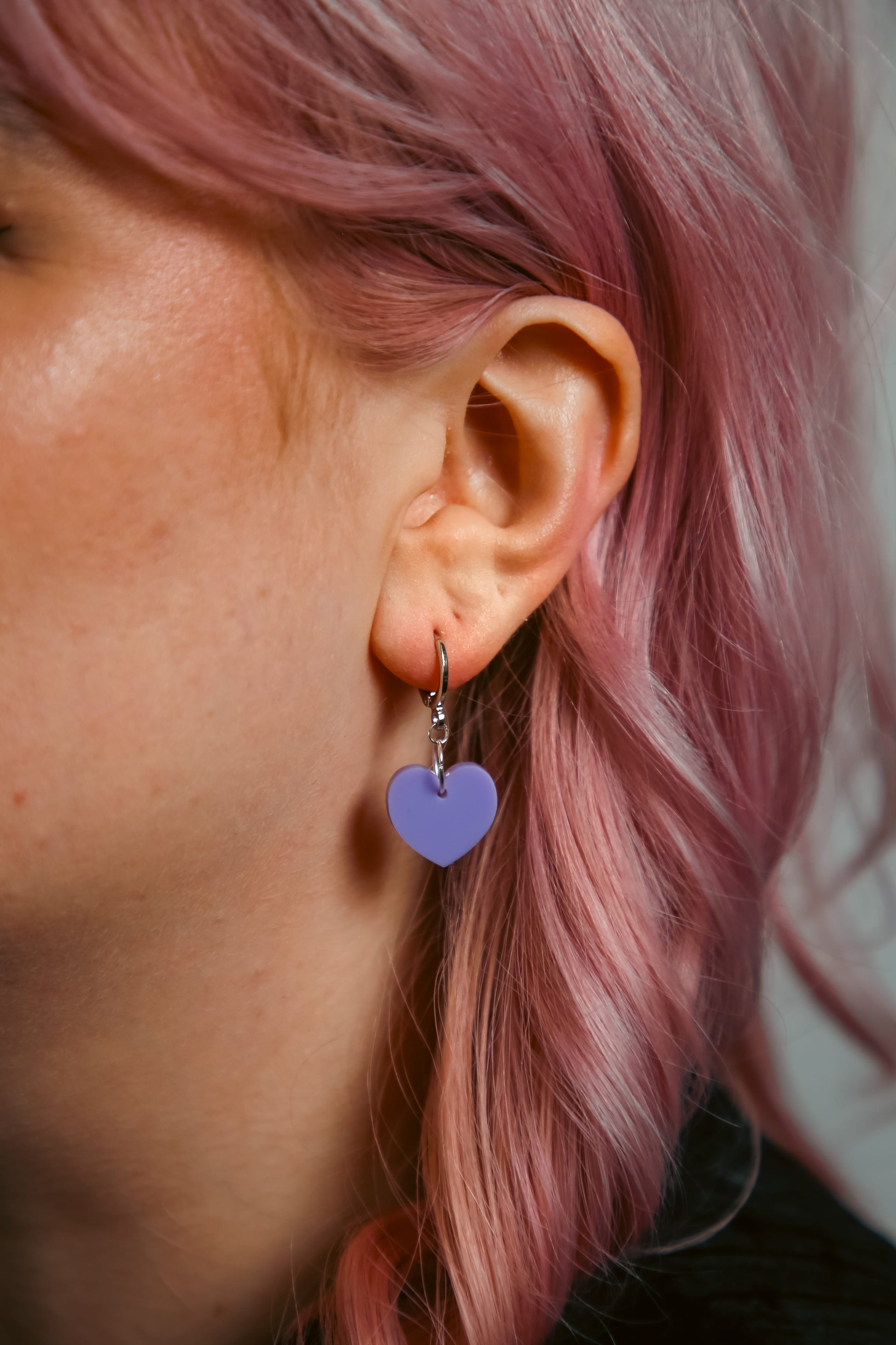 A pastel purple heart acrylic earring on an ear
