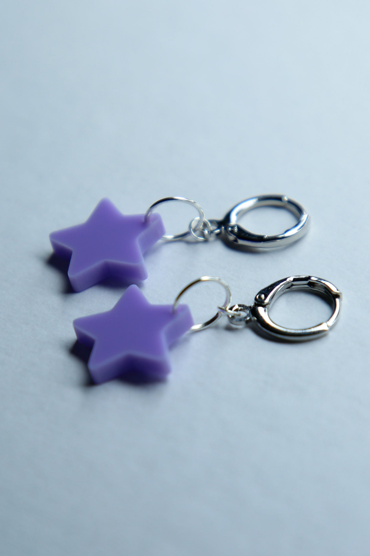 A pair of pastel purple star acrylic earring on a blue background