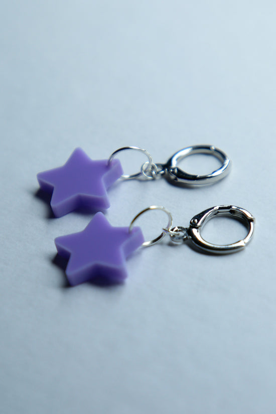 A pair of pastel purple star acrylic earring on a blue background